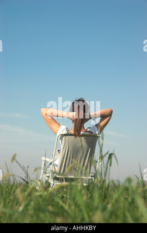 Junge Frau sitzend auf Stuhl im Bereich Arme hinter Kopf Rückansicht Stockfoto