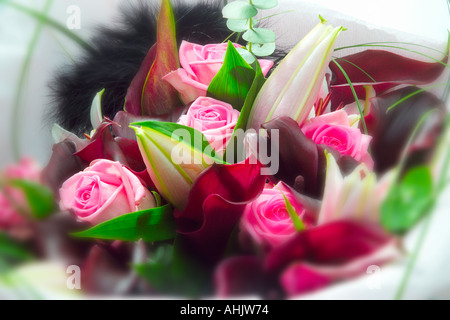Nahaufnahme eines Straußes aus rosa Rosen und dunkelroten Calla-Lilien, eingewickelt in weißes Taschentuch mit schwarzen Federn Stockfoto