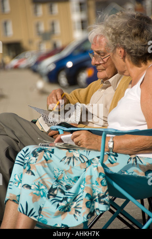 Älterer Mann tun Kreuzworträtsel mit Frau sitzen im Freien an Sommernachmittagen Aberystwyth, Wales Stockfoto