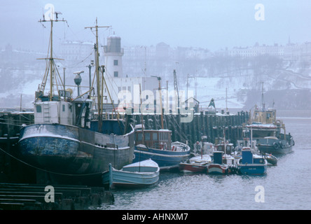 Scarborough Winterschnee auf Fischerboote, mit Leuchtturm hinter Scarborough, North Yorkshire, England, UK. Stockfoto