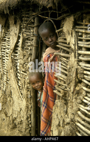 Ein Maasai Mädchen und ihre junge Schwester von der Tür ihre urige Hütte in der Nähe von Masai Mara National Reserve wüstenartigen gucken Stockfoto