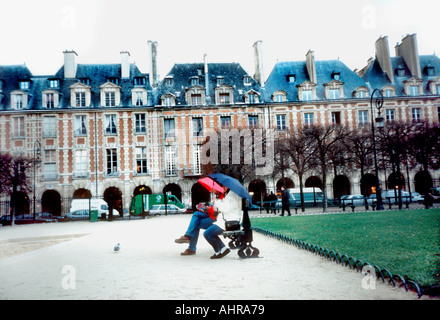 Paris Frankreich Parks Paar sitzt auf der Parkbank mit Sonnenschirmen im Regen 'Place des Vosges' Historic Architecture, Le Marais Stockfoto