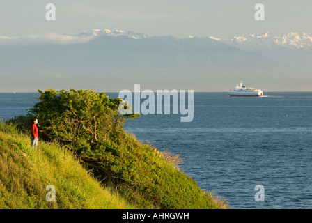 Eine Frau genießt die Aussicht vom Victoria es Dallas Straße Uferpromenade mit Olympic Mountains und Coho ferry im Hintergrund Stockfoto