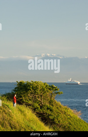 Eine Frau genießt die Aussicht vom Victoria es Dallas Straße Uferpromenade mit der Olympic Mountains und Coho im Hintergrund Stockfoto