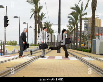 Geschäftsfrau und zwei Geschäftsleute Acrossdouble Straßenbahnlinien mit Koffern am Zebrastreifen läuft. Alicante, Spanien. Stockfoto