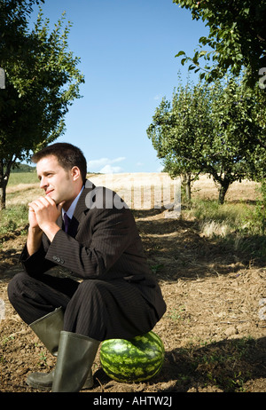 Mann sitzt auf Wassermelone im Obstgarten. Stockfoto