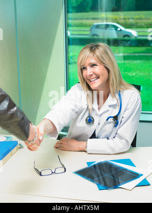 Ärztin an ihrem Schreibtisch Hand mit Patienten zu schütteln. Stockfoto