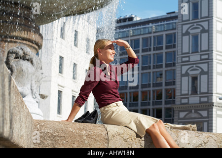 Geschäftsfrau auf Brunnen-Hand auf Stirn Blick in Ferne sitzen. Stockfoto
