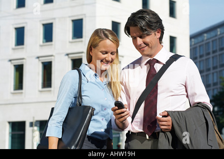 Geschäftsmann und Frau stehend auf dem Platz in der Stadt, beide sind auf der Suche auf mobile Display vor Lachen. Stockfoto