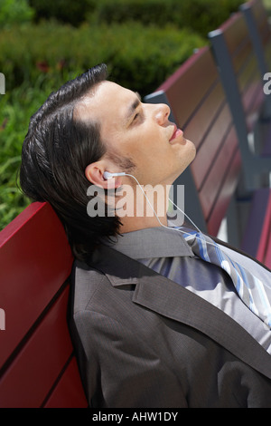 Geschäftsmann auf Bank mit MP3-Kopfhörern hören Augen dicht zugemacht. Stockfoto