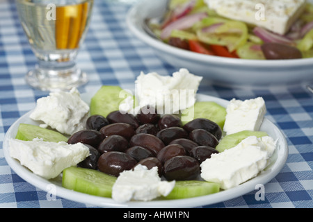 Platte mit Oliven, Feta und Gurke auf Tabelle griechischer Salat und Retsina im Hintergrund. Stockfoto
