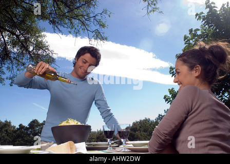 Junger Mann putting Olivenöl auf pasta Stockfoto