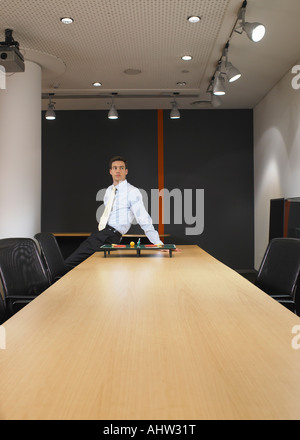 Porträt des jungen Mannes mit Miniatur-Tischtennis am Konferenztisch sitzen Stockfoto
