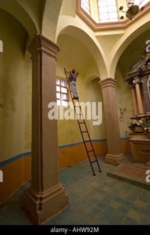 Ein Maler, hoch oben auf einer Leiter in einer Kirche (Mexiko). Peintre de Bâtiment Perché Sur Une Échelle Dans Une Église (Mexiko). Stockfoto