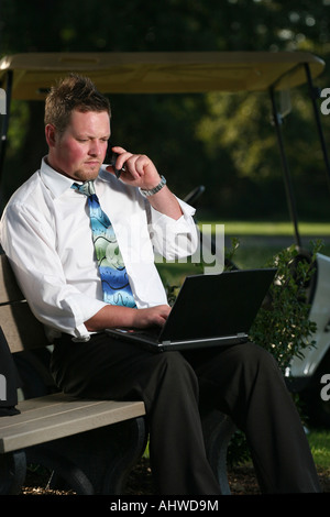 Der Mann Manager sitzt auf der Bank auf dem Golfplatz und ruft das Handy an und trägt Laptopbilder in den USA hochauflösende Bilder Stockfoto