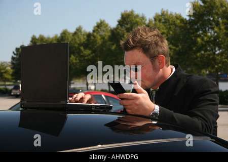 Der Managerin steht neben seinem Auto und ruft mit einem Laptop das Handy an, auf der Straße der Stadt Bilder horizontal in den USA hochauflösende Bilder Stockfoto