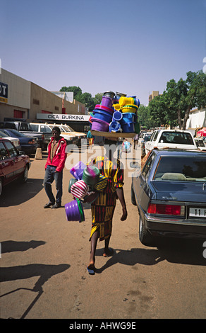 Weibliche Street Verkäuferin zu Fuß mit Kunststoff-Küche Waren auf ihrem Kopf. Ouagadougou, Burkina Faso Stockfoto