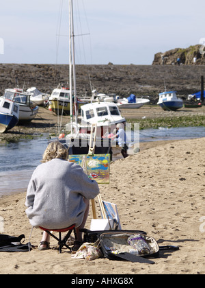 Mittlere gealterte Frau am Strand mit Farbe und Staffelei, Malerei der Boote im Hafen Stockfoto