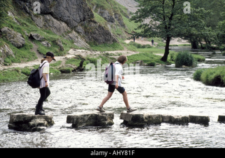 Wanderer mit Rucksack Rucksäcken überqueren Fluss Dove Trittsteine touristisch Dovedale Derbyshire Staffordshire Grenze im Peak District England Großbritannien Stockfoto