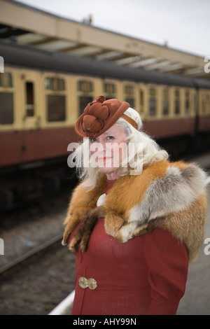 Reife Frau tragen Fox Pelz Stola Vintage Mode stehen auf Plattform warten auf Zug in Pickering Bahnhof, Yorkshire. Stockfoto