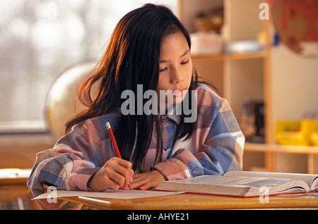 Asiatische amerikanische Studentin arbeiten mit Lehrbuch am Schreibtisch in der Mitte der Schule Klassenzimmer Stockfoto