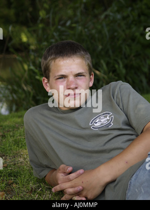 Teenager, Jeans und t-Shirt, Verlegung auf Rasen Bank neben einem Fluss suchen ernsthafte gerichtete Kamera Stockfoto