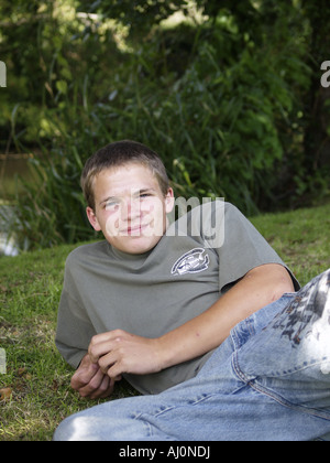 Teenager, Jeans und t-Shirt, ein Rasen-Bank neben einem Fluss, Handauflegen, lächelnd und Blick in die Kamera Stockfoto