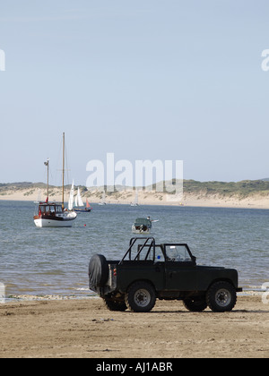 Black off Road Fahrzeug parkte direkt am Meer an einem Sandstrand. mit Booten und Yachten im Hintergrund Stockfoto