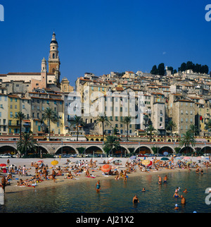 Überfüllten Strand mit Schwimmer und Menschen im Liegestuhl unter bunten Sonnenschirmen in der alten Stadt von Menton Südfrankreich Stockfoto