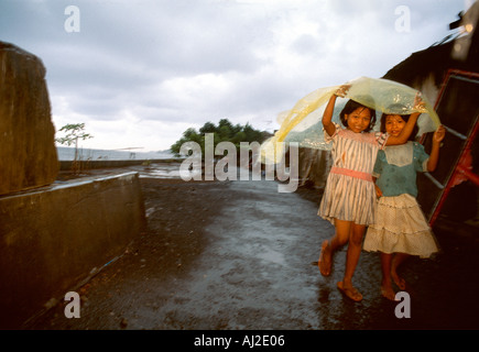 Bali-Kinder im Regen. Zwei glückliche kleine Mädchen zu Fuß in der Monsun-Regen, Regenzeit in Singaraja, Bali, Indonesien. Stockfoto