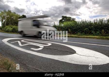 Ein verschwommener weißer Lieferwagen saust vorbei ein 30 km/h-Grenze-Schild gemalt auf einer Landstraße. Stockfoto