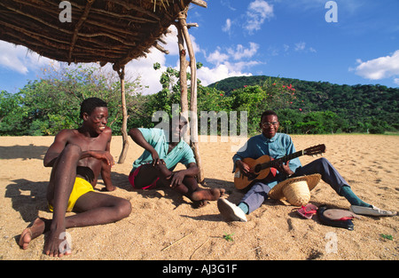 Zwei malawische Kerle entspannende und Hören zu einem jungen Freund seine Gitarre spielen auf einem Strand am Lake Malawi, Malawi. Stockfoto