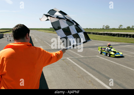 Marshall in orange Kostüm, wehende Zielflagge am Ende Superkart Rennen Bishopscourt Schaltung Grafschaft, Nord-Irland Stockfoto