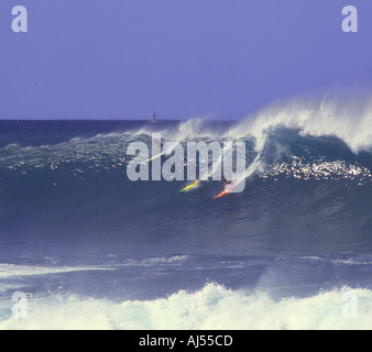 Drei Surfer ausziehen auf eine fünfzehn Fuß Riesenwelle in Waimea Bay mit Yacht Segeln im Hintergrund Nordküste Oahu Hawaii Stockfoto