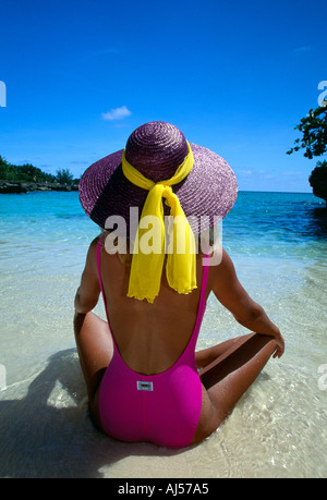 Grand Cayman Sandbar Frau in rosa Anzug lila Hut sitzt am Strand von hinten erschossen Stockfoto