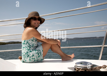 Mit blumigen Kleid und Hut sitzt auf Kreuzfahrt-Schiff in Port Stephens New South Wales NSW Australia KMH lächelnde Frau Stockfoto