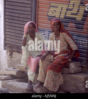Zwei schöne indische Frauen tragen traditionelle indische Saris sitzen außerhalb eines geschlossenen Ladens in Jaisalmer, Indien. Stockfoto