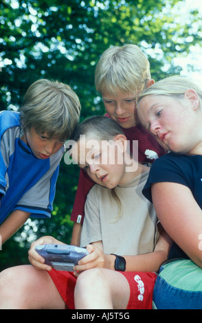 ein kleiner Junge spielt mit seinem Gameboy mit drei anderen Kindern beobachtete ihn Stockfoto