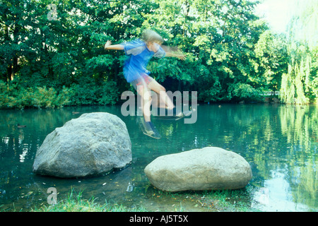 kleiner Junge einen Sprung von einem Felsen in einem Teich zu einem anderen Stockfoto