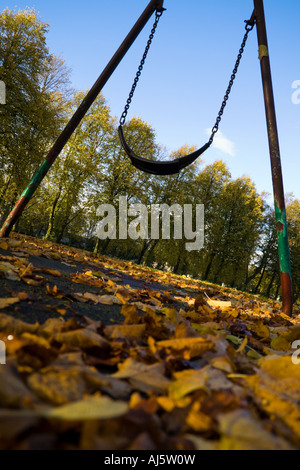 Leere Swing im Park mit Herbstlaub auf dem Boden. Stockfoto