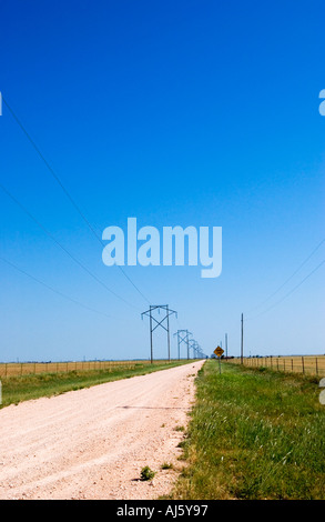 Gerade, unbefestigte Straße, gesäumt von Stromleitungen unter klarem Himmel in den ländlichen USA. Stockfoto