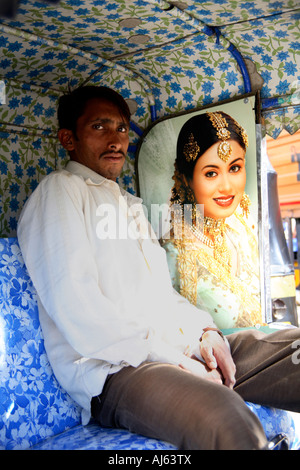 Indian Auto Rickshaw Fahrer posiert neben dem Plakat der eleganten indischen Prinzessin im hinteren Teil seiner floralen Kabine, Junagadh, Saurashtra, Indien Stockfoto