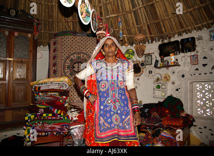 Harijan Tribal Frau umgeben von Lager von Kunsthandwerk und Stickerei in ihrer Schlammhütte in Ludia Village, nr Khavda, Kutch Bezirk, Gujarat, Indien Stockfoto