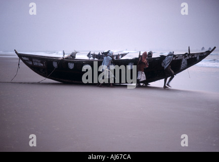 Fischer, die ihr Boot vom Strand entfernt in der Morgendämmerung starten Stockfoto