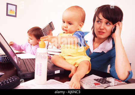 Frau sitzt am Schreibtisch mit ihren Kindern beim Telefonieren und mit ihrem Laptop. Stockfoto