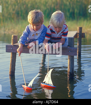 kleine Jungen und Mädchen spielen auf Dock mit Spielzeug Segelboote Stockfoto