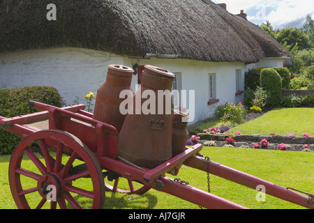 Milchkannen auf einem Holzkarren außerhalb Reetdachhaus Adare County Limerick Irland Stockfoto