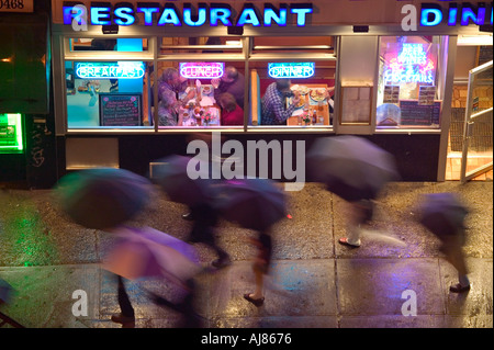 Menschen mit Regenschirmen an regnerischen Abend vorbei an alle Nacht Diner an der Eighth Avenue an der 48th Street in Midtown Manhattan New York Stockfoto