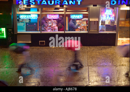 Menschen mit Regenschirmen an regnerischen Abend vorbei an alle Nacht Diner an der Eighth Avenue an der 48th Street in Midtown Manhattan New York Stockfoto