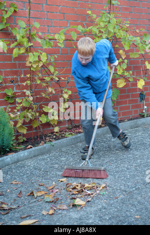 ein kleiner Junge fegt Blätter in seiner Familie Garten hinter dem Haus Stockfoto